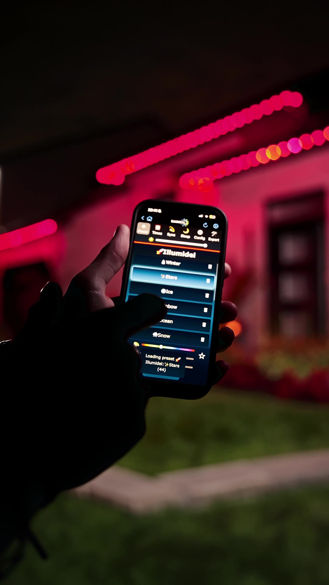 L’application Illumidel dans la main, maison illuminée derrière